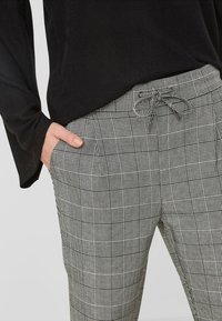 Grå rutiga byxor med dragsko i midjan, med ett rutmönster och sidofickor, i kombination med en svart långärmad topp.