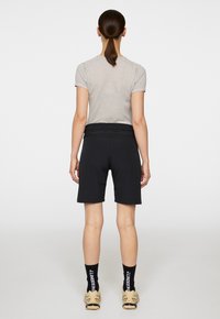 Musta shortsit venyvää kangasta, joissa on tiukka vyötärö, yhdistettynä vaaleanharmaaseen, teksturoituun lyhythihaiseen paitaan, nähtynä takaa.