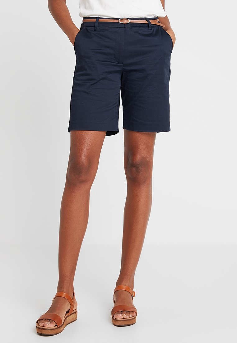 Un short bleu marine avec une coupe ajustée et des poches latérales, associé à une ceinture en cuir marron et des sandales à plateforme marron.
