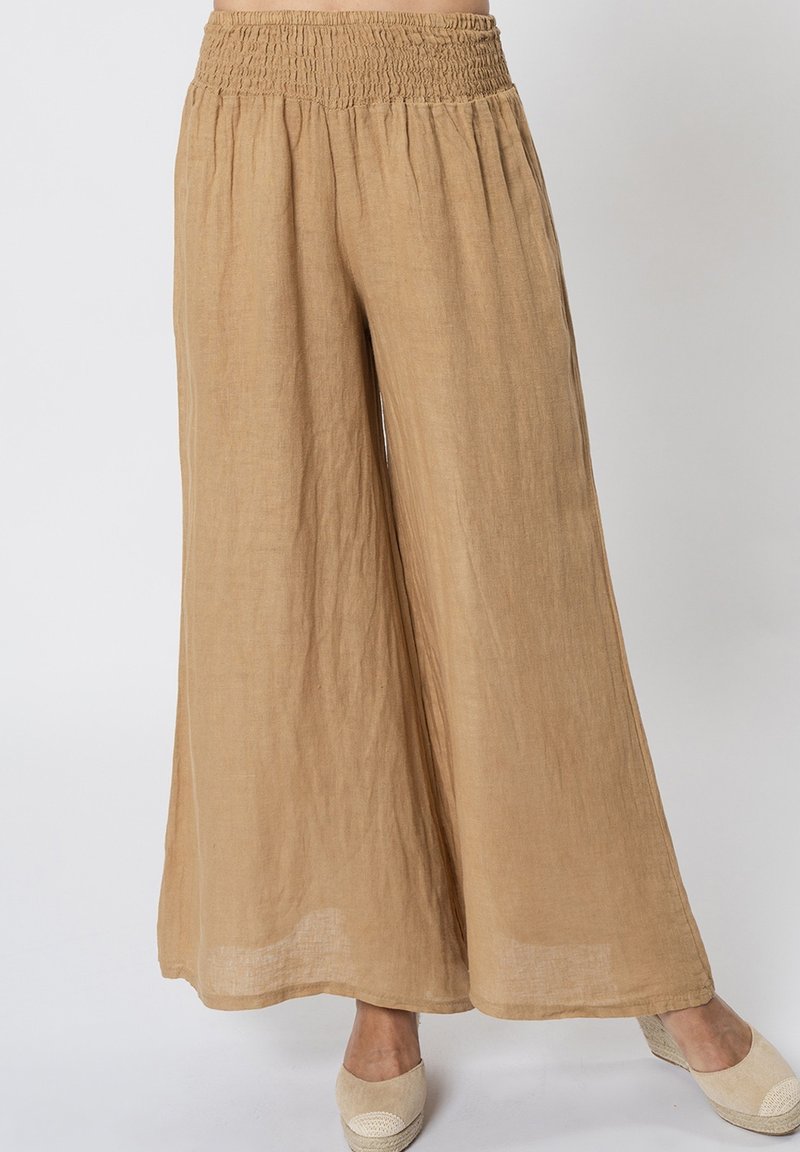 Pantaloni in lino beige a gamba larga con una vita arricciata e una finitura morbida e strutturata. Accentuati da calzature leggere e casual.