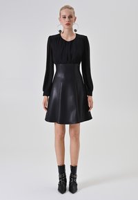 Zwarte jurk met een aansluitende taille en een uitlopende rok. Lange, gepofte mouwen. Paar zwarte enkellaarsjes met gestudde accenten.