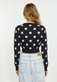 Maglione nero a maglia con un motivo floreale in bianco e viola, con un design cropped e polsini a costine. Indossato con jeans azzurri chiari.
