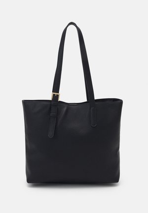 Zwarte leren tote bag met een structuur, voorzien van twee schouderbanden, waarvan één met een kleine gouden gesp, tegen een eenvoudige lichte achtergrond.