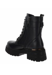 Stivale alla caviglia in pelle nera con suola robusta, lacci e zip laterale. Presenta dettagli metallici e una texture vicino al tallone.
