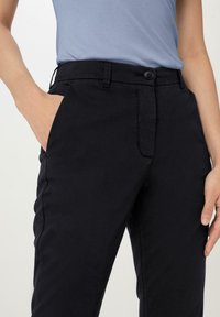 Černé slim-fit kalhoty s hladkou texturou, zapínání na jeden knoflík a boční kapsy. Nosit s světle modrým topem.