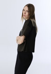 Top cropped nero con maniche corte, caratterizzato da una texture liscia e accenti scuri a contrasto. Il modello posa di lato su uno sfondo chiaro.