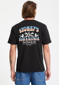 Czarna koszulka bawełniana z kolorową retro grafiką i napisem "Stoney's Tow & Repair" na plecach, ozdobiona narzędziami i elementami designu.
