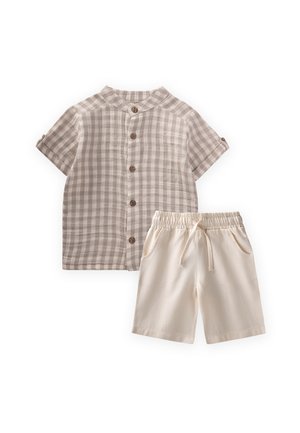 Beżowa koszula na guziki z krótkim rękawem w kratę oraz kremowe szorty ze ściągaczem ułożone na płasko na białym tle.