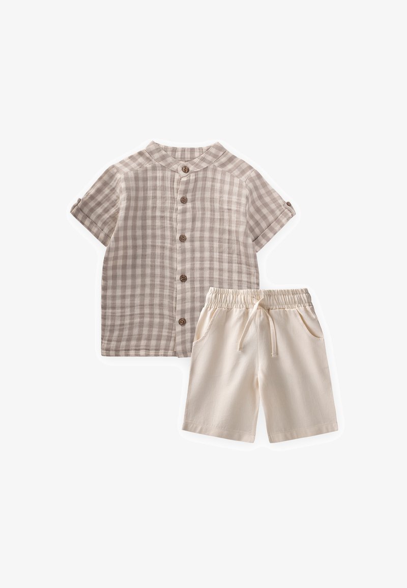 Chemise beige à manches courtes à carreaux avec boutons et short crème à cordon, disposés à plat sur un fond blanc.