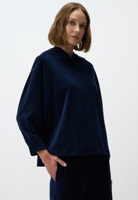 Navyblauw hoodie met een relaxte pasvorm, geribbeld textuur, verlaagde schouders en subtiele zijsplitten, gecombineerd met bijpassende broeken.