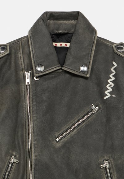 Zwarte leren motorjas met zilverkleurige hardware, inclusief ritsen en drukknopen. Heeft een uniek ontwerp met een zigzagaccent.