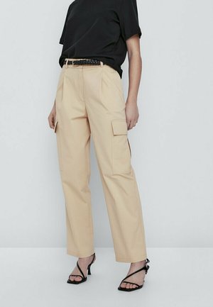 Woman wearing beige cargo pants with side pockets, black braided belt, black short-sleeve top, and black strappy heeled sandals.