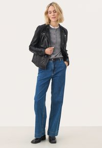 Veste de motard en cuir noir, chemise grise à boutons et jeans larges bleus. Des bottines noires complètent la tenue. Design minimaliste avec des caractéristiques classiques.