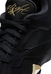 Svart sneaker med mocka och mesh-material, med gulddetaljer. Skosnörena är vävda och det finns en perforerad design på ovansidan.