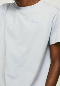 Jasnoniebieska bawełniana koszulka z okrągłym dekoltem i krótkimi rękawami. Wyszywane logo "Pepe Jeans" w jasnym niebieskim kolorze na piersi. Gładka faktura.