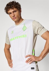 Biele krátke rukávy s svetlošedými rukávmi, zdobené zelenými akcentmi, vertikálnymi pruhmi a výrazným logom "MATTH'AI".