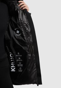 Fekete Khujo dzseki fényes belsővel, logókkal és vízálló anyagból. Belső oldalán részletes ápolási útmutató található.