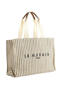 Canvas shoppingväska med svarta vertikala ränder på en krämfärgad bakgrund, med läderdetaljer och dubbla tyghandtag. "LE MARAIS PARIS" tryckt.