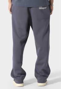 Pantalons de survêtement gris avec une coupe décontractée, arborant un petit logo blanc à l'arrière, fabriqués dans un tissu doux au toucher lisse.