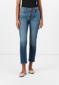 Blauwe spijkerbroek met een aangesloten taille, rechte pijpen en omgeslagen broekspijpen. Gecombineerd met lichtroze ballerina's en een zwarte mouwloze top.