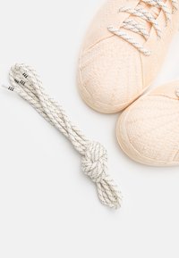 Baskets rose clair texturées avec dessus tissé et semelles en caoutchouc, accompagnées de lacets noués blancs à rayures grises.