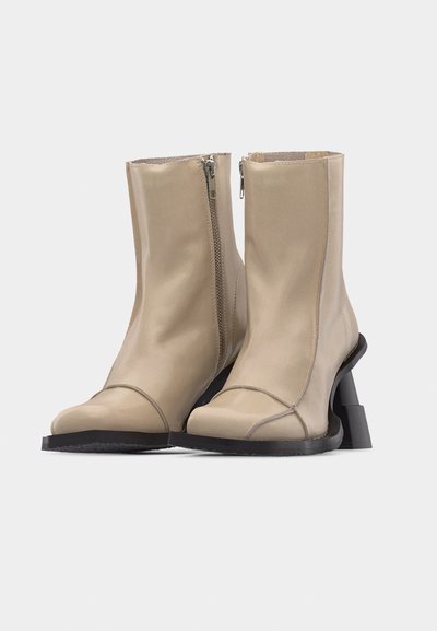 Μπεζ δερμάτινα μποτάκια αστραγάλου με πλαϊνά φερμουάρ, τετράγωνα δάχτυλα και μαύρα γωνιακά τακούνια με φαρδιά βάση σε λευκό φόντο.