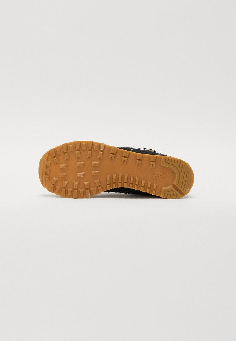 Semelle de chaussure de sport noire avec une surface en caoutchouc texturé et des crampons prononcés, dotée d'une semelle extérieure brun clair contrastante.