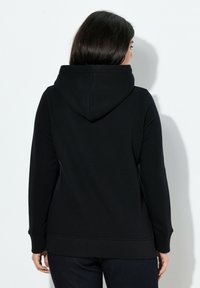 Sudadera negra con bolsillo canguro, puños y dobladillo acanalados. Material suave con una textura blanda y una costura única que recorre la espalda.