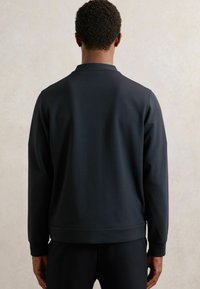 Felpa nera con colletto rotondo, maniche lunghe, texture liscia e orlo aderente. L'immagine mostra la parte posteriore senza logo o motivi.
