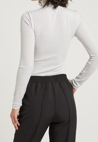 Silbernes Langarmoberteil mit hohem Kragen, aus einem schimmernden Stoff gefertigt. Kombiniert mit schwarzen, elastischen Hosen mit geradem Bein.