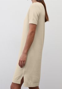 Abito in maglia beige con maniche corte, polsini a costine e spacchi laterali. Texture liscia e vestibilità morbida, che arriva a metà coscia.