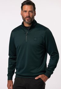 Pullover corto verde scuro con chiusura a zip e maniche elastiche, realizzato in tessuto liscio e dotato di un colletto alto, con un piccolo logo sul petto.