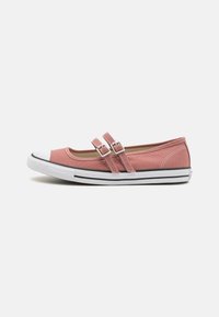 Zapatilla de lona rosa con correas de doble hebilla, puntera y suela de goma blanca, presenta una franja negra a lo largo de la base, textura suave.