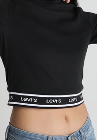 Svart kortärmad turtleneck sweatshirt med en vit och svart märkesresårband i fållen, figursydd design och slät textur.