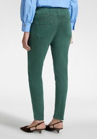 Pantalones verdes ajustados con una textura suave, cinturilla elástica y dos bolsillos traseros, combinados con sandalias de tacón marrones.