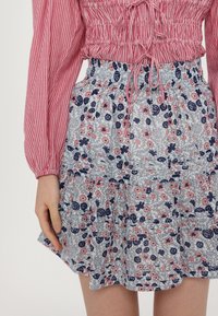 Blomstrete lagdelt skjørt i lyseblått med rosa og marineblå blomster. Har elastisk midje og volangkant. Sammen med en rødstripete topp.