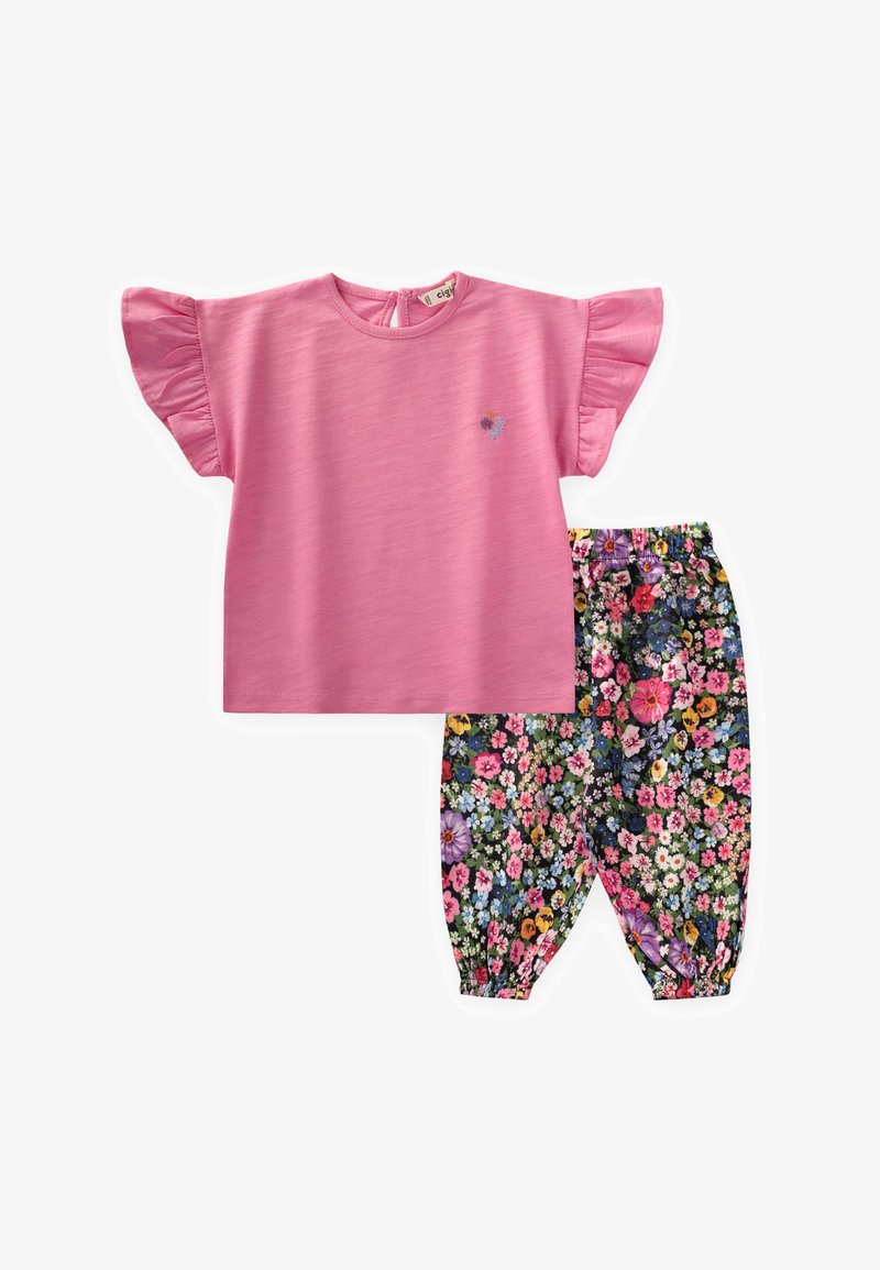 Top corto a maniche corte di un luminoso colore rosa, con maniche arricciate, abbinato a pantaloni con stampa floreale che presentano una varietà di fiori colorati su uno sfondo scuro.