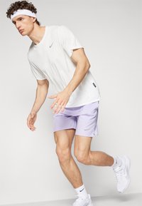White, textured athletic shirt and light purple shorts with a silver Nike logo. White sneakers and a white headband complete the outfit.