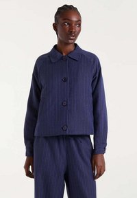 Chaqueta de rayas marinas con cuello redondeado, cinco botones oscuros y mangas raglán. Textura suave, diseño corto acompañado de pantalones a juego.