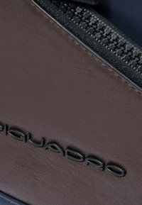 Scarpa di pelle marrone con superficie testurizzata, una cerniera nera e un logo nero in rilievo. Il design enfatizza linee pulite e funzionalità.