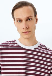 Camiseta de rayas burdeos con rayas horizontales blancas, de cuello redondo y mangas cortas, hecha de un suave material de algodón.