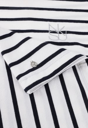 Witte stof met zwarte horizontale strepen toont een opgevouwen mouw met een kleine ronde zilveren knoop en geborduurde initialen bij de halslijn.