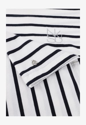 Witte stof met zwarte horizontale strepen toont een opgevouwen mouw met een kleine ronde zilveren knoop en geborduurde initialen bij de halslijn.