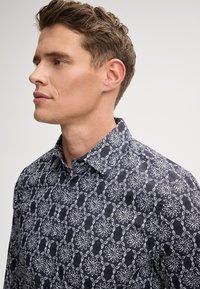 Marineblauw shirt met een witte bloemenpatroon, button-down kraag en korte mouwen. Gemaakt van lichte stof met een zachte textuur.