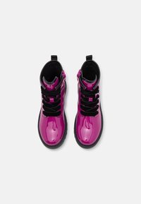 Botas de tobillo de charol púrpura con cordones negros, un cuello negro y tiras para facilitar el calzado. Presentan una suela texturizada y un acabado liso y brillante.