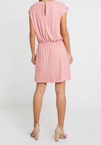 Kort rosa klänning med avslappnad passform, elastisk midja och en liten nyckelhålssmyckning på baksidan. Tillverkad av ett glansigt, lätt material.