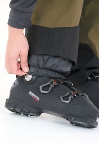 Sort skistøvle med tekstureret overflade og røde og sølvfarvede detaljer, med justerbare spænder og en tætsiddende gaiter omkring anklen.