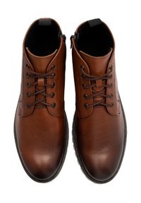Brązowe skórzane botki sięgające kostki o gładkiej teksturze, okrągłym nosku i sznurowanym zapięciu. Posiadają kontrastowe przeszycia i czarną pętelkę.