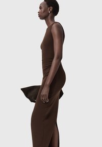 Brązowa dopasowana sukienka maxi z wysokim dekoltem, bocznym rozcięciem i bez rękawów. Wykonana z gładkiego, elastycznego materiału, zapewniającego smukłą sylwetkę.
