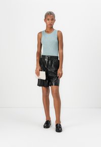  Lichtblauw geribd tanktop, zwarte leren shorts en zwarte instappers. Houdt een gestructureerde beige clutch vast. Eenvoudig modern ontwerp.